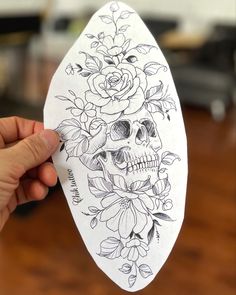 a person holding up a piece of paper with a skull and flowers on it