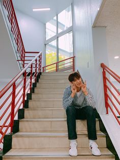 a young man sitting on the stairs in front of a red railing and white shoes