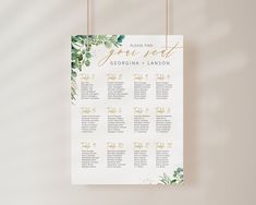 a wedding seating chart with greenery and gold foil lettering on a hanger against a neutral background