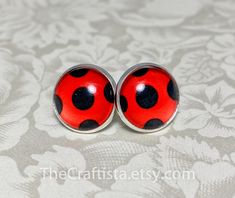 pair of red and black ladybug stud earrings on white fabric with floral design