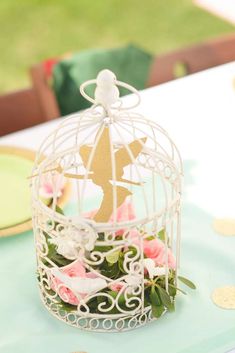 a white birdcage filled with pink flowers on top of a blue table cloth