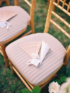 two folding chairs with fan on them sitting in the grass next to flowers and greenery