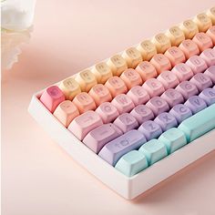 a colorful keyboard sitting on top of a table next to a white flower and pink background