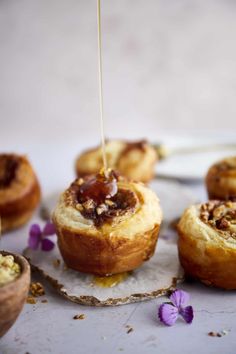 some food is being drizzled with honey on the top and purple flowers around it