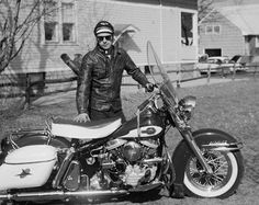 a man standing next to his motorcycle in front of a house on the side of the road