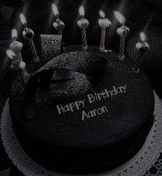 a black birthday cake with lit candles on it and the words happy birthday aaron written in white