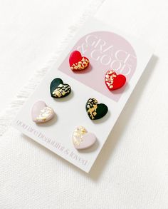 four heart shaped studs on top of a white card with gold foiling and glitter