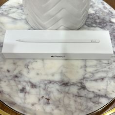 an apple pencil sitting on top of a marble table next to a white ceramic vase