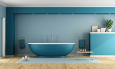 a bathroom with blue walls and wooden flooring is pictured in this image, there is a freestanding bathtub on the far wall