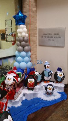 a group of penguins that are standing in front of a christmas tree with balloons on it