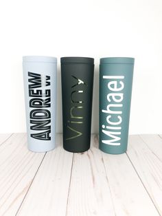 three travel mugs sitting next to each other on a wooden table with white walls