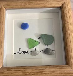 two birds sitting next to each other in a shadow box with the word love written on it