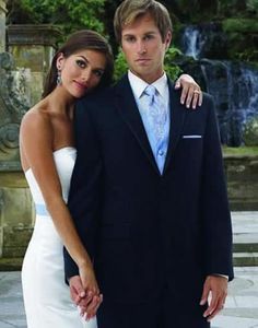 a man and woman standing next to each other in front of a fountain wearing formal attire