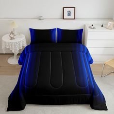 a bed with black and blue sheets in a room next to a white table,