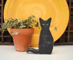 a black cat sitting next to a potted plant and yellow plate on a table