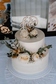 a three tiered cake with flowers and the word love on top is sitting on a table