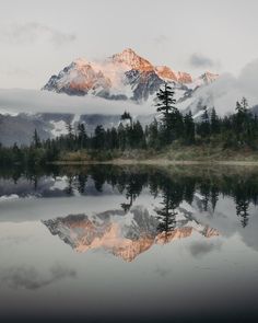 the mountains are covered in clouds and trees as they reflect in the still lake water