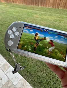 a person holding up a video game device in their hand while standing on the grass