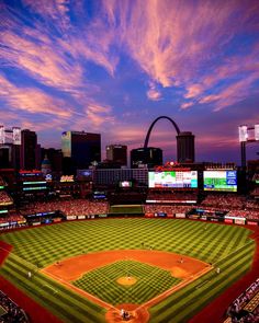 a baseball stadium with the st louis arch in the background at sunset or sunrise time