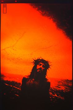 a man with a crown of jesus on his head in front of an orange sky