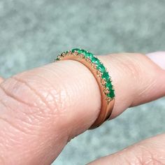 a close up of a person's hand with a ring on their finger that has green stones in it