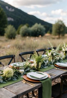 an outdoor table set with place settings and greenery