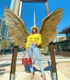 a woman standing in front of a large angel statue with her hands on her hips