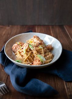 a white bowl filled with pasta and meat on top of a blue napkin next to a fork