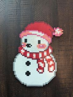 a snowman made out of perler beads on a wooden table with a red hat and scarf