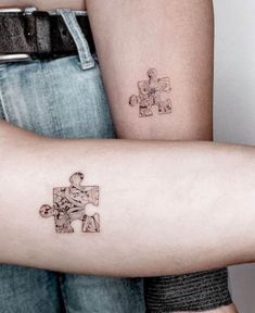 two people with matching tattoos on their arms holding each other's arm and one has a puzzle piece