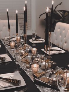 a table set with silver and gold christmas decorations, black napkins, candles and plates