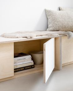 a book shelf with books and a pillow on top of it in front of a white wall