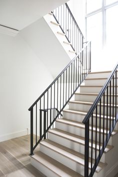 there is a white staircase with black railings in the room and light coming through the window