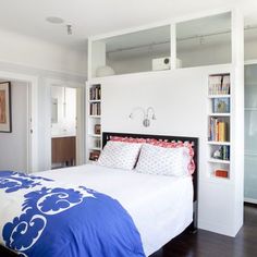 a bed with blue and white comforter in a bedroom next to bookshelves