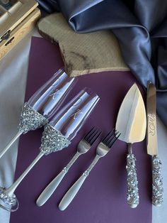 five silver colored utensils are sitting on a purple table cloth next to a blue napkin