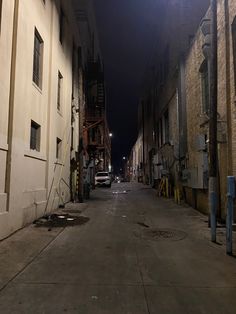 an empty street at night with cars parked on the side and buildings in the background