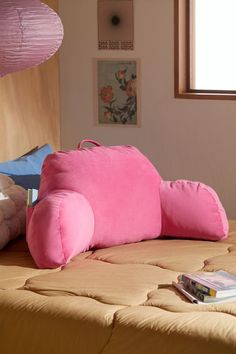 a pink pillow sitting on top of a bed next to a book and some pillows