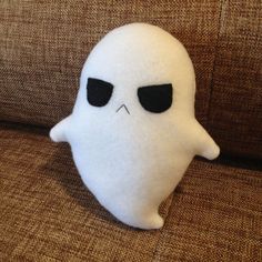 a white stuffed ghost sitting on top of a brown couch next to a black eye patch