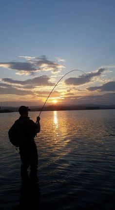 a man standing in the water while holding a fishing rod and wearing a backpack at sunset