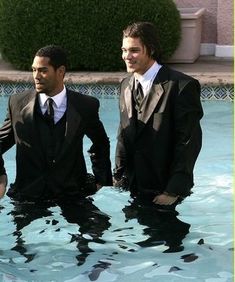 two men in suits are standing in the water