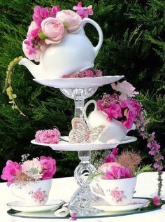 three tiered cake stand with pink flowers and teacups on the top, surrounded by greenery