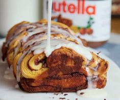 a cinnamon roll with icing sitting on top of a white plate next to a jar of nutella