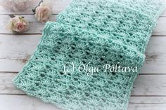 a green crocheted blanket sitting on top of a white wooden table next to flowers