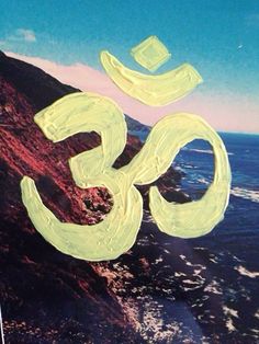 an om sign painted on the side of a mountain next to the ocean in front of a blue sky