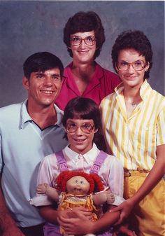 a family posing for a photo in front of a gray background with the child holding a doll