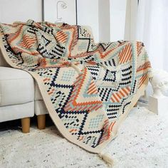 an orange and blue blanket sitting on top of a couch next to a white chair