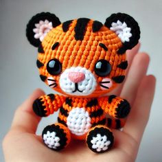 a small crocheted tiger doll sitting on top of someone's hand in front of a white background