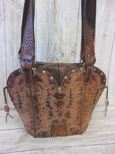 Infuse your look with a dose of Santa Fe style with this one-of-a-kind leather handbag. Hand-crafted from up-crafted cowboy boots and belts. Tote style with no pockets No two alike, signed and numbered Magnetic closure and metal concho detail Measures approximately 10"x12"x5" This exquisite leather bag is more than just a cowboy boot purse - it's a wearable work of art that celebrates the spirit of the American West. Perfect for the lady who wants to infuse her look with a dose of Southwestern s Western Bags With Concho Detail, Western Style Bags With Concho, Western Brown Bags For Rodeo, Western Style Brown Bags For Rodeo, Western Style Brown Bag With Concho, Western Style Hand Tooled Brown Bag, Brown Leather Bags For Rodeo, Hand Tooled Brown Bags For Rodeo, Hand Tooled Brown Bag For Rodeo