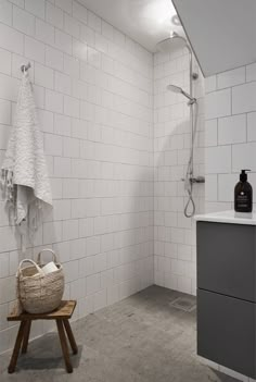 a white tiled bathroom with a wooden stool and shower head mounted on the wall next to it