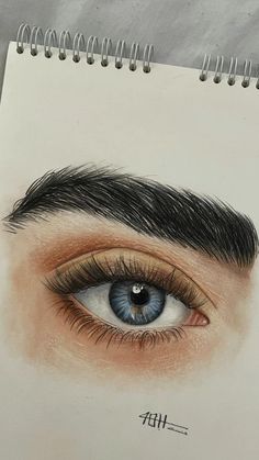 a drawing of an eye with long lashes and blue eyeshade, on top of a spiral notebook